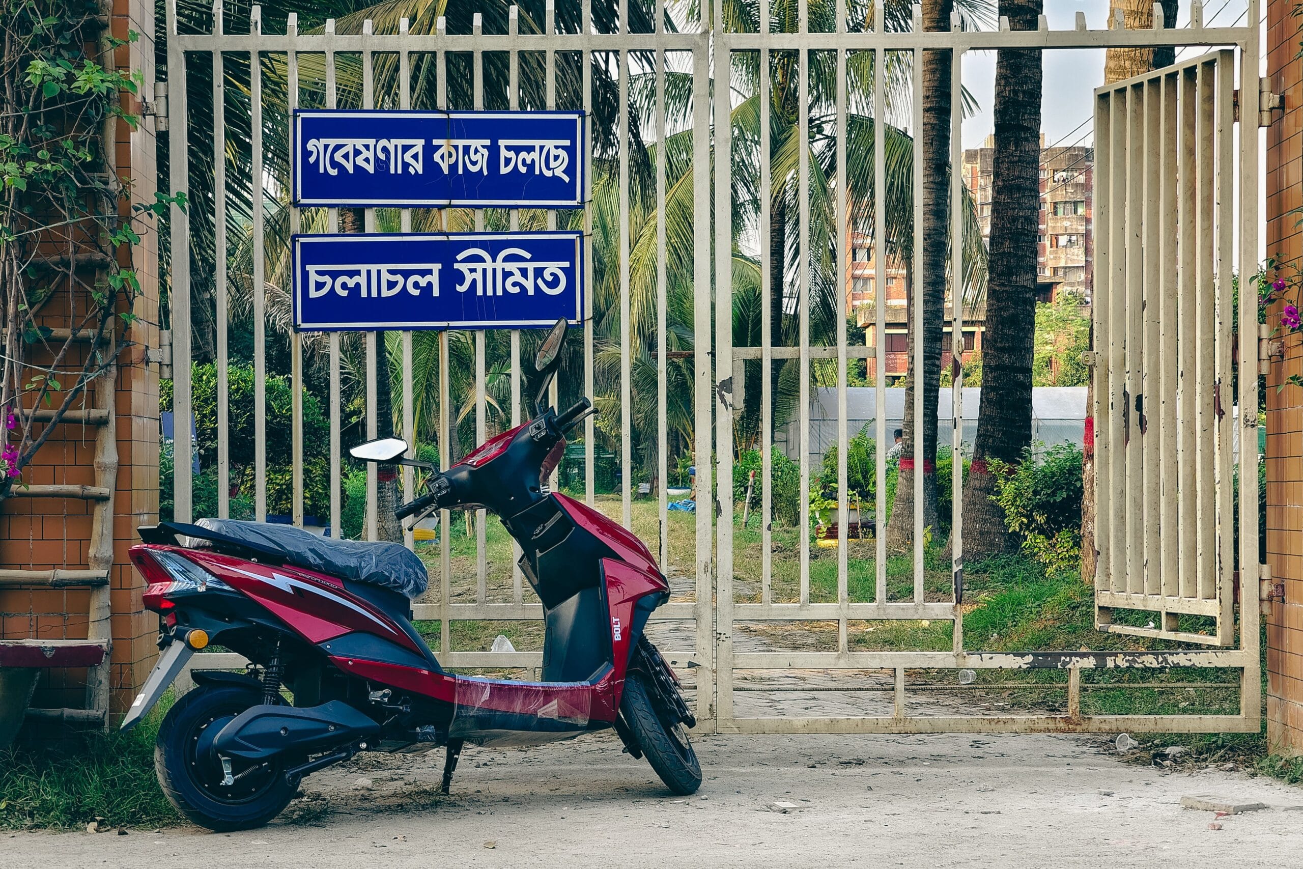 Electric Two-Wheelers in India illustration showing a maroon electric scooter parked outside a white gate with Bengali signs