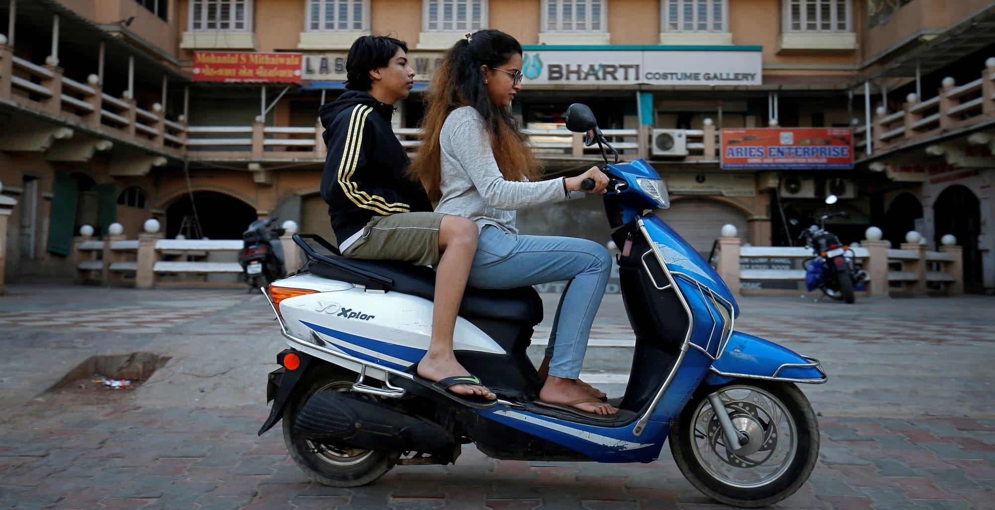 Electric Two-Wheeler Report illustration showing two young people riding a blue and white YO Bykes electric scooter in India